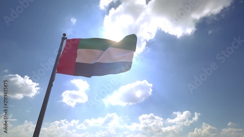 UAE Flag waving on a Flagpole from a Moving Angle in front of a blue sky with clouds	