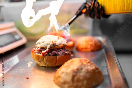 Bild auf Leinwand A chef uses a blowtorch to melt cheese on a gourmet pulled pork burger