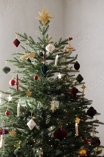 Beautiful Christmas tree decorated with paper toys, candles and gold star topper. Vintage Christmas tree decor, Scandinavian holiday style, warm festive mood.
