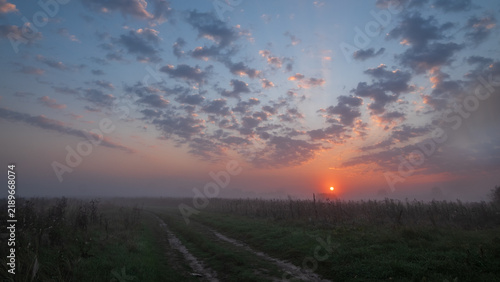 Fotografie A beautiful morning landscape shows a vibrant sun rising over a misty field, wit