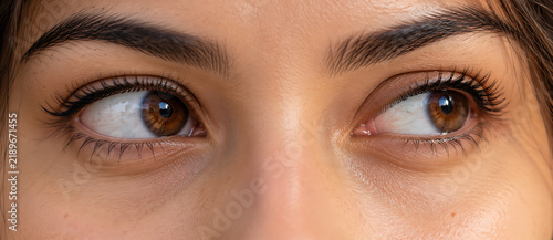 Close up photograph showcases a pair of brown eyes looking upwards with detailed eyelashes