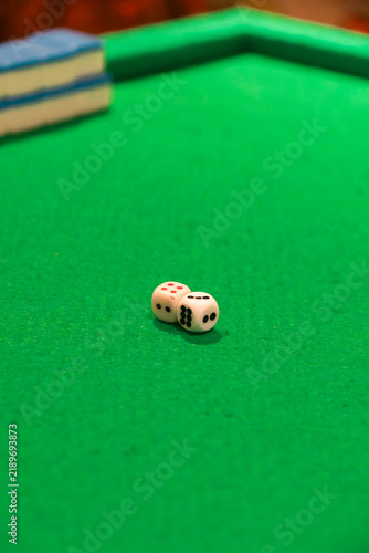 Roll of the Dice: Two white dice showing a total of three rest on a green felt surface, with a cue ball and chalk in the background, suggesting a game in progress.