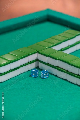 Mahjong Tiles and Dice on Green Felt: A close-up view of green and white mahjong tiles arranged on a green felt table, with two translucent blue dice resting nearby, suggesting a game in progress.