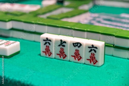 Mahjong Tiles on Green Table: Four Chinese Mahjong tiles with red character inscriptions are neatly arranged on a green felt surface, showcasing a moment of play in this classic tile-based game.