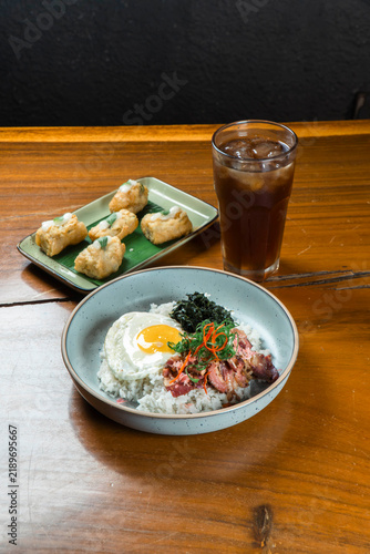Savory Bowl and Refreshment: A delicious meal served in a ceramic bowl, featuring rice, a fried egg, and toppings, accompanied by a plate of fried snacks and a glass of iced beverage.
