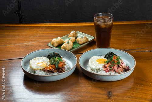 A Culinary Delight: Two bowls of delicious rice topped with savory meat, fried egg, and fresh greens are served alongside a plate of golden fried snacks and a refreshing iced tea.