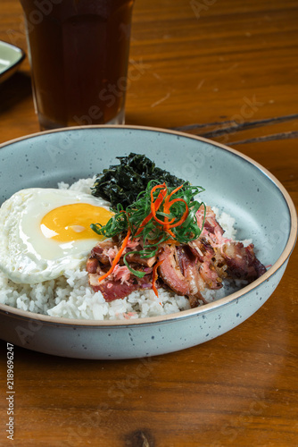 Savory Rice Bowl Delight: A delicious and satisfying rice bowl featuring a perfectly fried egg, succulent meat, and fresh greens, served with a side of iced tea.