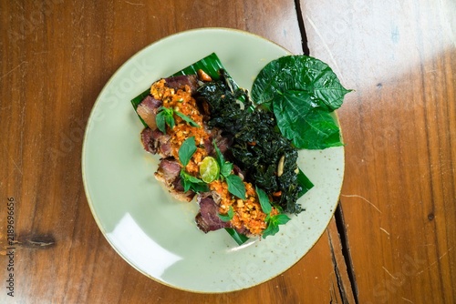 Savory Delight: A meticulously prepared dish featuring tender meat slices, crispy fried herbs, and fresh greens, served on a light green plate atop a rustic wooden table.