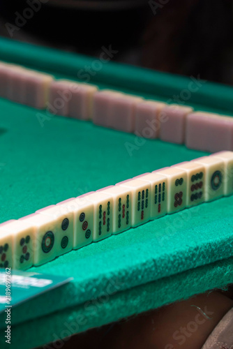 Mahjong Game Board: Close-up of a green felt mahjong table with rows of mahjong tiles arranged for a game, showcasing the intricate details of the tiles and the game setup.