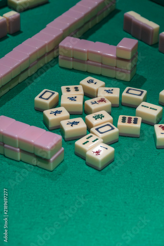 Mahjong Game Set: An assortment of Mahjong tiles, predominantly pink and cream colored, are scattered across a green felt surface, suggesting an ongoing game or preparation for play.