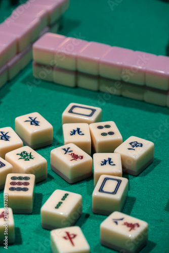 Mahjong Tiles on Green Felt: A close-up shot of scattered mahjong tiles, each intricately carved with distinct symbols, resting on a vibrant green felt surface, ready for a game.
