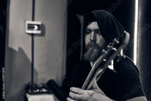 Obraz na plátně Bearded male bassist playing during rehearsal in dark studio with monochrome lig