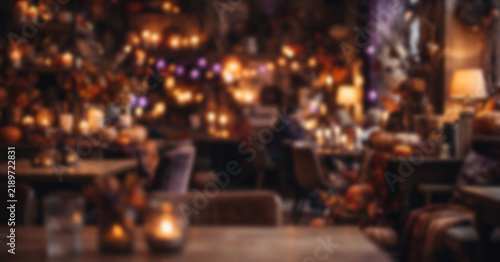 Cozy Halloween café background featuring fully blurred pumpkins, warm lamps, autumn decorations, and soft orange purple bokeh for elegant seasonal designs.