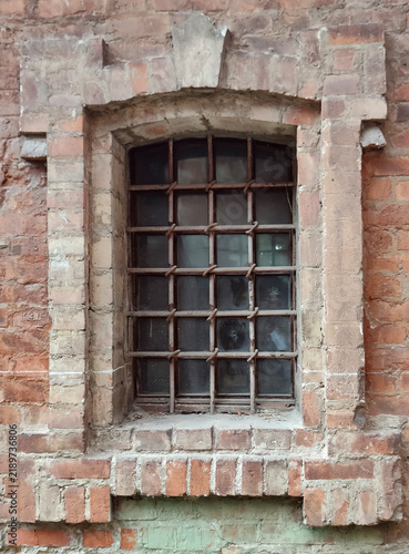 Weathered brick wall with an arched barred window and aged metal grille
