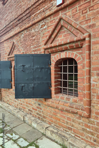 Weathered brick facade with barred window and metal shutters
