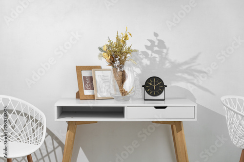 White desk with aesthetic interior design. A table in a room with a clock, photo frames, and chairs. 