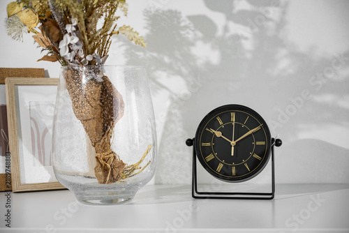 Analogue clock and flowers in a vase on the table in the room.
