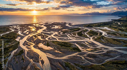 Braided river estuary landscape winding through sandbanks towards sunset ocean.
