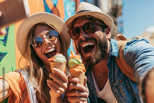 Happy couple holding ice cream cones and taking a selfie outdoors in front of colorful wall