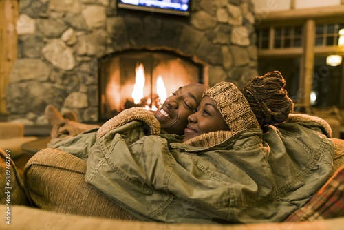 Happy couple relaxing together wrapped in a warm blanket near a cozy indoor stone fireplace