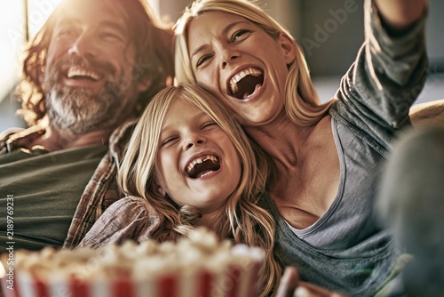 Happy family laughing together while watching a movie with popcorn at home on the couch