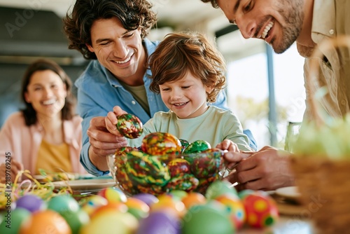 Happy family with young son painting colorful easter eggs together at home