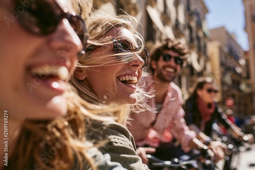 Happy friends riding bicycles together through a historic city street on a sunny afternoon ride
