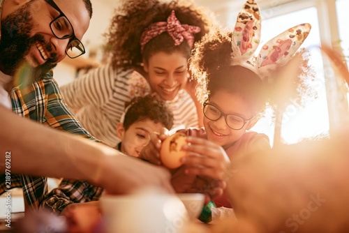 Happy multicultural family painting easter eggs together at home in the warm spring sunlight