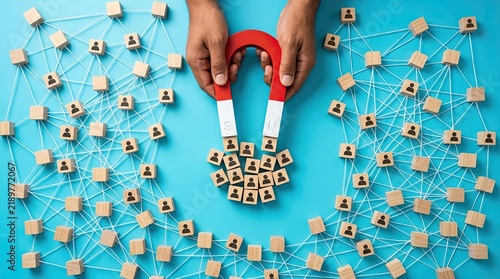 Hands using magnet to attract connected wooden block figures in network pattern on blue background with figures linked lines network layout solid magnet pulls communication visualization abstract