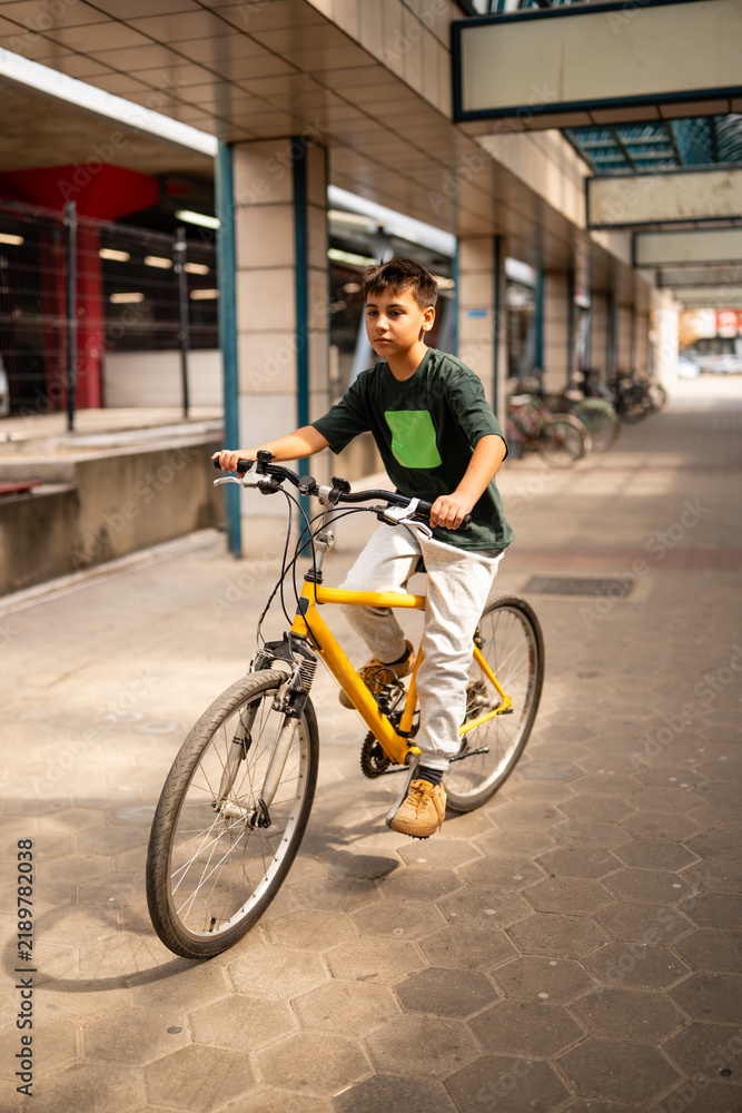 Fototapeta premium Boy riding yellow bicycle outdoors in urban environment