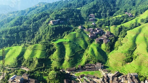 High angle view of Longji rice terraces with green layered fields and traditional wooden houses in Guilin under bright sunlight.