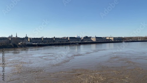 View of the Garonne River in Bordeaux, France, with historic buildings lining both sides of the waterfront. The scene highlights the relationship between the river, historic architecture, and Bordeaux