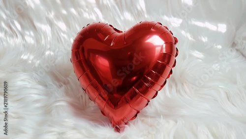 Ultra-high-fidelity 4K romance concept clip showing a glossy metallic red heart balloon resting softly on a thick white cloud of faux fur ideal for Valentine s Day advertisements