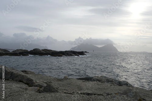 Rocky coastline with waves crashing against stones, distant islands visible under a cloudy sky in Lofoten Islands, Norway during the month of September
