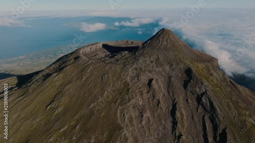 Aerial view of the impressive volcanic crater at the summit of Mount Pico, Azores, showing the rugged geological formations, steep slopes, and the surrounding sea of clouds.