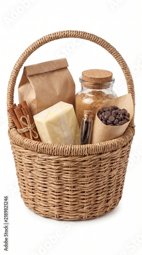 Woven grocery basket filled with baking ingredients including brown sugar cinnamon sticks butter and chocolate chips for holiday desserts on a white background.