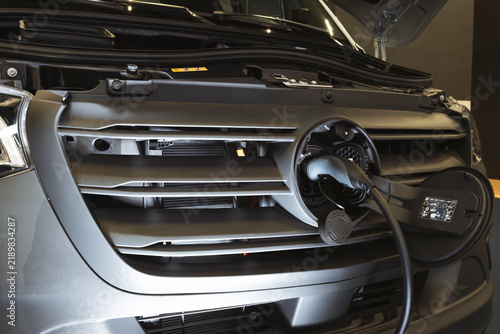 Close-up of an electric vehicle's charging port with plug connected, integrated into the front grille panel.