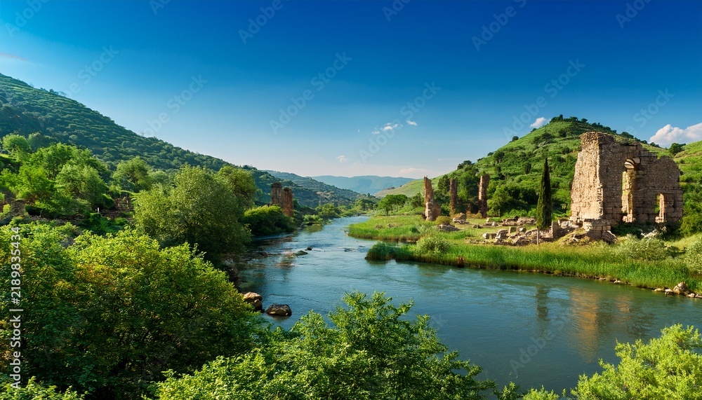 Fototapeta premium Views Of A River Flowing Between Hills With Green Trees And Ruins Seen Under A Clear Sky