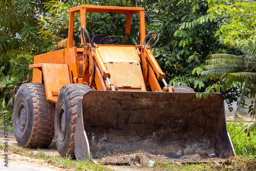 Fotografía Vintage orange front-end wheel loader parked outdoors, surrounded by lush green