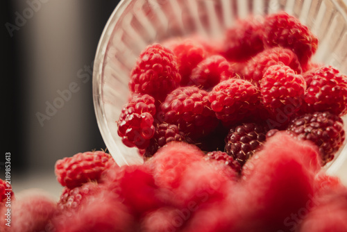 фотографія Fresh red raspberries spilling out of a glass bowl close up view