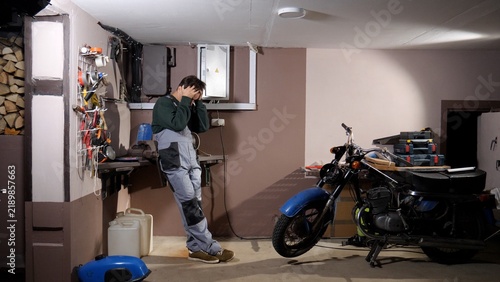 Картината върху платно Mechanic in overalls covering his face with hands in a cluttered workshop, frust