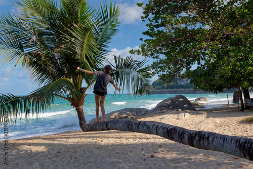 Young woman balancing on leaning coconut palm tree trunk on tropical beach

