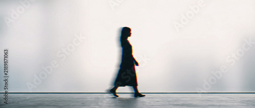 Blurry silhouette of a woman walking against a bright white background