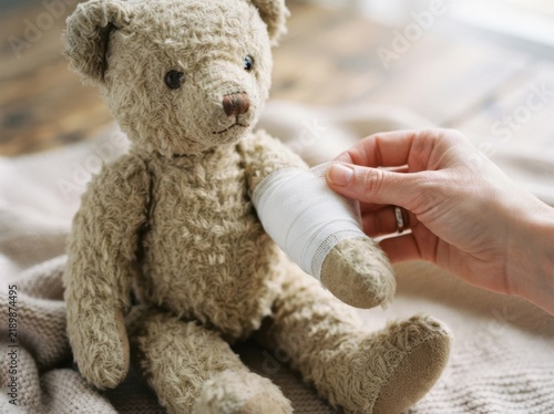 A caring hand bandaging the injured arm of a fluffy stuffed teddy bear toy representing child healing and recovery