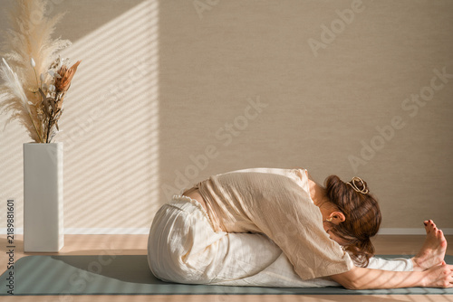 Foto ヨガマットで深く前屈して脚を伸ばす女性。柔軟性を高めるヨガとストレッチ習慣