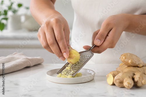 Hands grating fresh aromatic ginger root on small ceramic grater