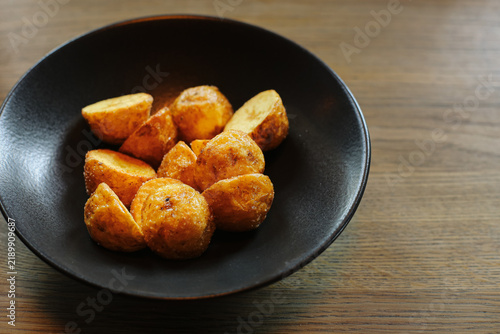 Foto Roasted potato wedges in black bowl on wooden table background