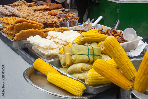 Obraz na plátně Boiled corn on the cob, pamonha, and coconut sweets cocada displayed at a traditional Brazilian street food stall