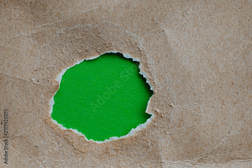 Konstfotografi torn hole in kraft paper revealing green background for teaser campaigns, hidden messages, investigations concepts