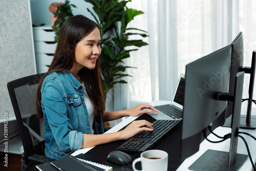 Obraz na płótnie Smiling young Asian IT developer working software development information on pc screens and laptop, creating program coding for latest version application on website with firmware updated. Stratagem.